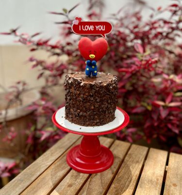 Torta de chocolate con trocitos de chocolate, relleno de manjar y fudge, decorada con figura 3D en fondant del personaje Tata de BTS.