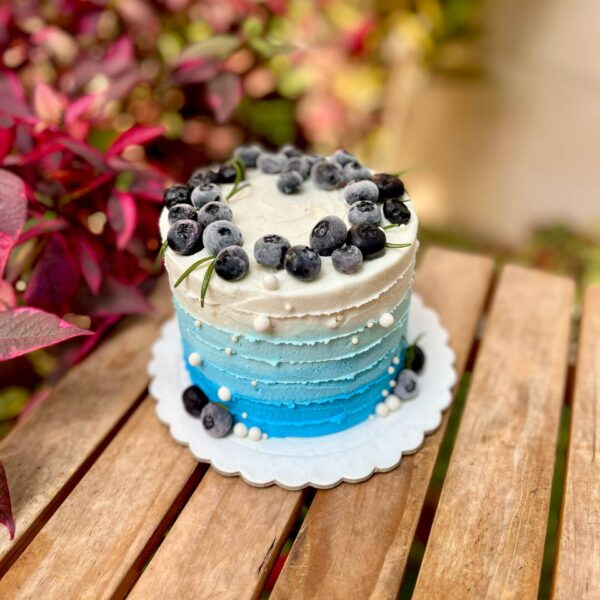 Torta pequeña decorada con buttercream en tonos blanco y celeste, adornada con arándanos frescos, ramitas de romero y perlitas comestibles, ideal para regalar en el Día del Padre.