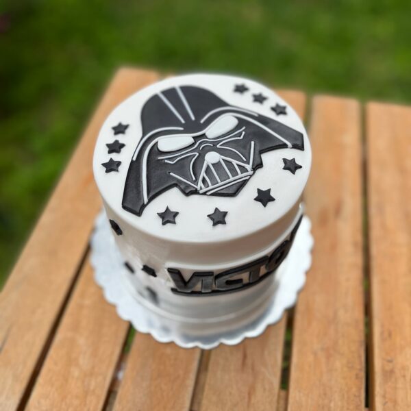 Torta de un piso con acabado en fondant, decorada con el logo de Darth Vader en la parte superior y estrellas alrededor.