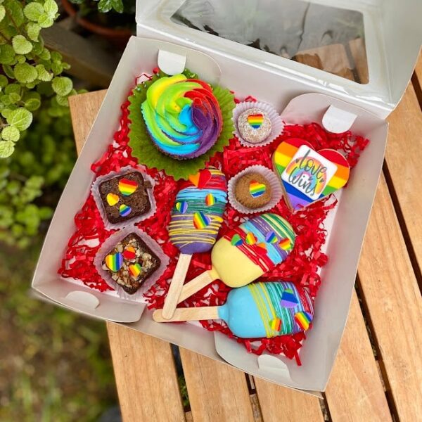 Box sorpresa temática Pride con cupcake, brownies, trufas, alfajor y lacypops decorados con colores de la bandera del orgullo.