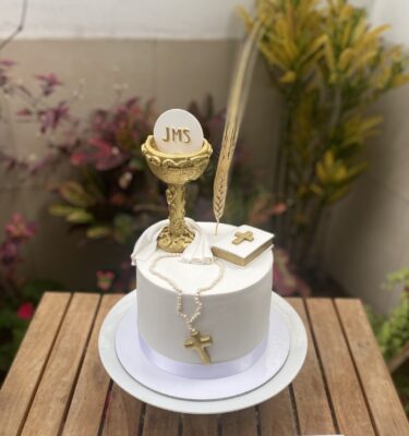 Torta de bautizo decorada con fondant, incluyendo un cáliz, rosario y biblia modelados a mano sobre la superficie.