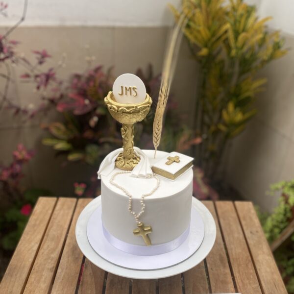 Torta de bautizo decorada con fondant, incluyendo un cáliz, rosario y biblia modelados a mano sobre la superficie.