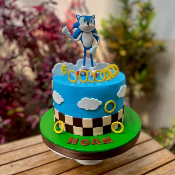 Torta temática de Sonic, cubierta en fondant azul, decorada con Sonic en 3D en la parte superior y aros dorados de fondant alrededor.