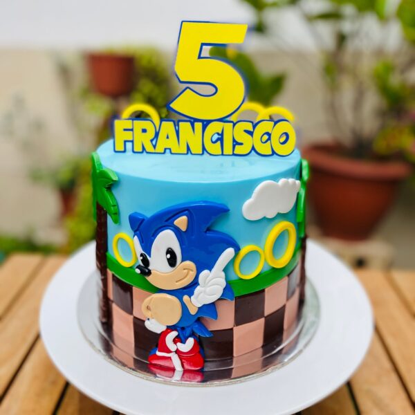 Torta de Sonic en fondant con detalles de palmeras, aros dorados, línea de carrera y figura 2D de Sonic.