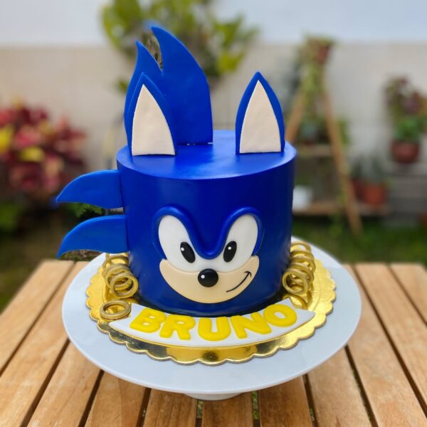 Torta de un piso cubierta en fondant azul que simula el rostro de Sonic, con detalles en fondant para los ojos, orejas y hocico, decorada en la base con aros dorados inspirados en el videojuego.