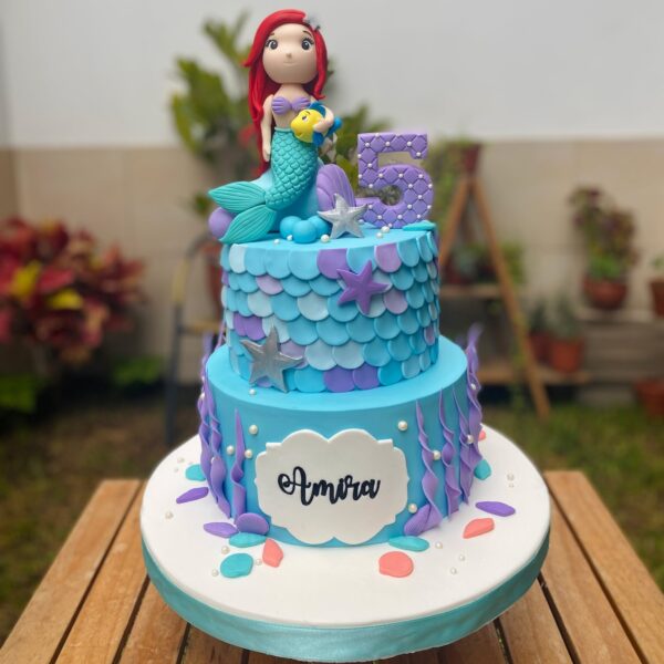 orta de dos pisos inspirada en La Sirenita, con figuras en fondant de Ariel y Flounder, y detalles marinos decorativos.