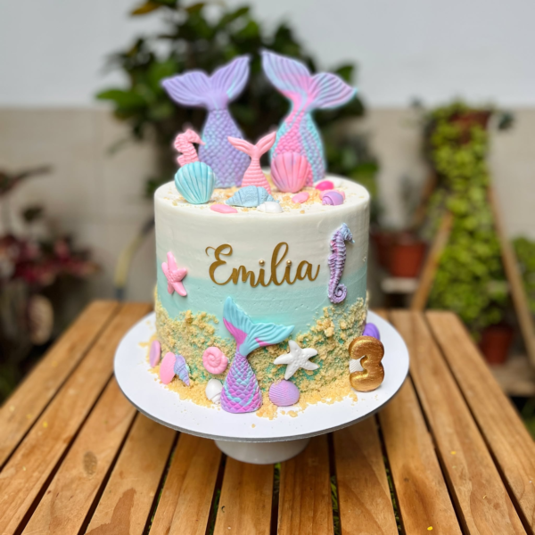 Torta de un piso decorada con buttercream en tonos marinos, colas de sirena en fondant y detalles de estrellas de mar, conchitas y corales.