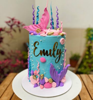 Torta de un piso decorada con buttercream y detalles marinos en fondant, como colas de sirena, conchitas, estrellas de mar y algas.