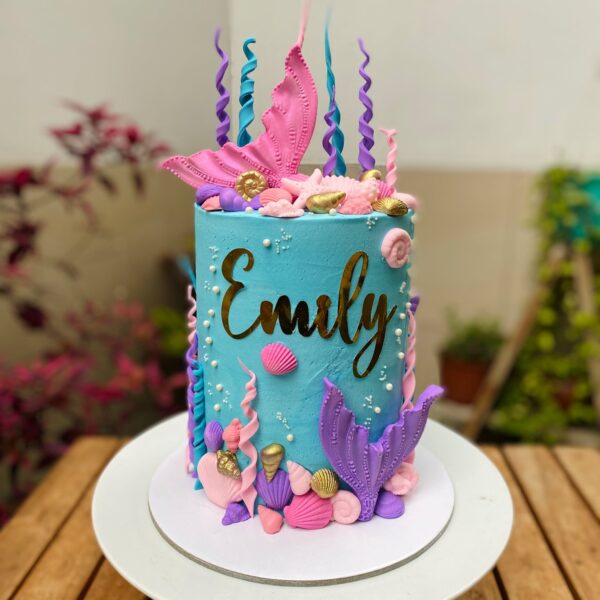 Torta de un piso decorada con buttercream y detalles marinos en fondant, como colas de sirena, conchitas, estrellas de mar y algas.