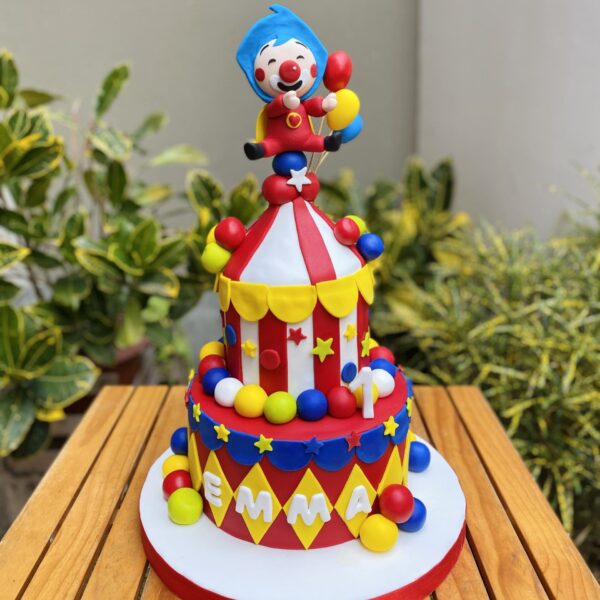 Torta de dos pisos con temática de circo, decorada completamente en fondant. En la parte superior está Plim Plim, con colores vivos y detalles inspirados en un show infantil lleno de alegría.