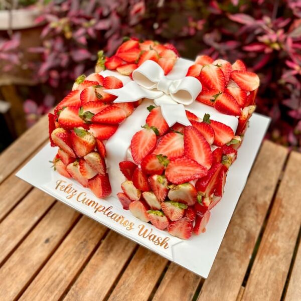 Torta cuadrada decorada con fresas frescas y un elegante moño al centro.