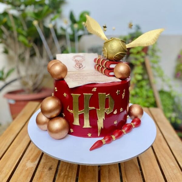 Torta de Harry Potter de un piso, forrada en fondant y decorada con elementos icónicos del mundo mágico: carta de Hogwarts, varita mágica, Snitch dorada, libros y esferas decorativas, todo elaborado en fondant.