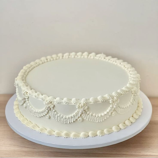 Torta de boda circular bañada en buttercream, decorada con un topper de iniciales en dorado o plateado.