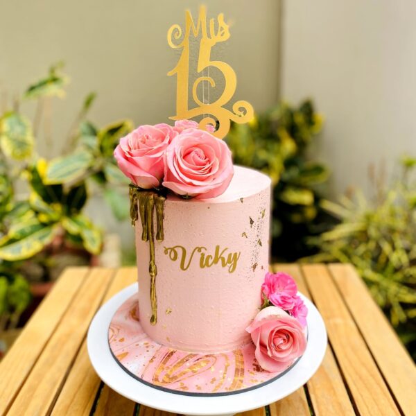 Torta de un piso bañada en buttercream con drip dorado, flores naturales y topper personalizado en dorado.