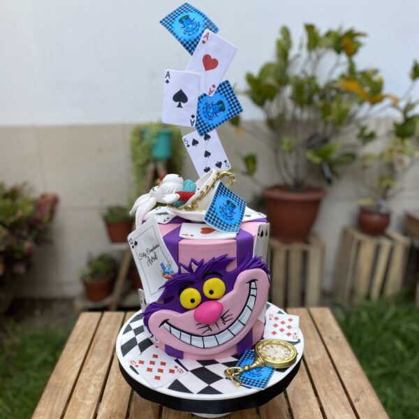 Torta de un piso de Alicia en el País de las Maravillas, forrada en fondant, con el gato sonriente en 2D al frente, el conejo en 3D en la cima y decoración de naipes en papel de arroz.