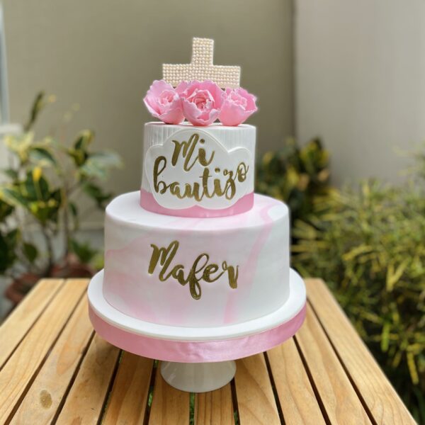 Torta de dos pisos para bautizo, decorada en fondant rosa mármol con rosas de azúcar, cruz hecha de perlitas, marco de fondant con la frase "Mi Bautizo" y nombre personalizado.