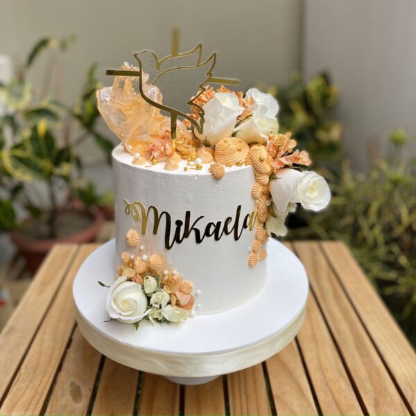 Torta de Primera Comunión de un piso, bañada en buttercream con rosetones, flores naturales, caramelo decorativo moderno y topper de silueta del Espíritu Santo.