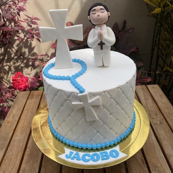Torta de un piso con acabado capitoné en fondant, decorada con un niño modelado en 3D de azúcar, cruz y rosario en fondant, y personalización de nombre.