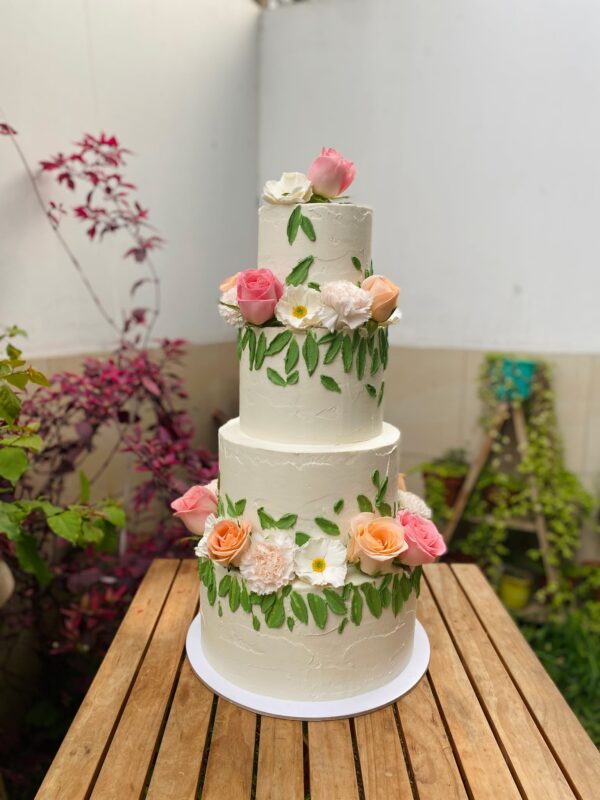 Torta de tres pisos para quinceañero, decorada con hojas de buttercream verde y flores naturales variadas en cada nivel.