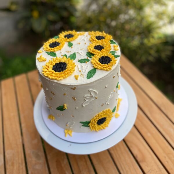 Torta bañada en buttercream, decorada con girasoles de buttercream en la parte superior y en los laterales.