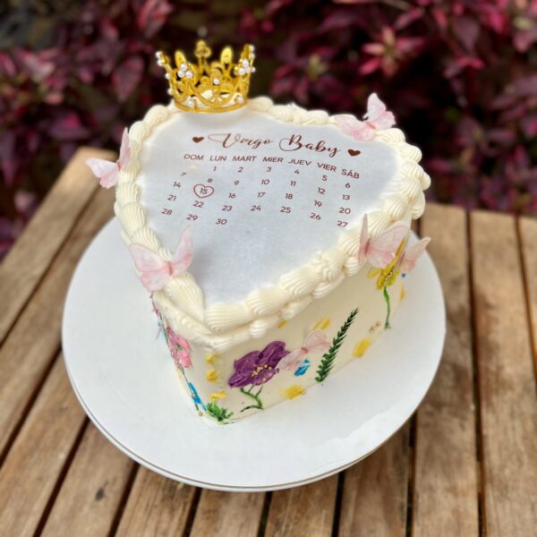 Burncake en forma de corazón, decorado con flores en buttercream en tonos delicados y una corona de bisutería brillante que le da un toque elegante y especial.