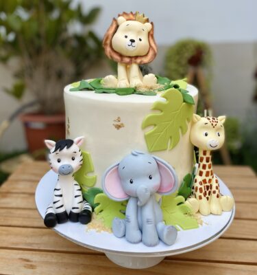 Torta temática safari de varios pisos decorada con animales 3D en fondant: un león en la cima y una jirafa, elefante y cebra en la base.
