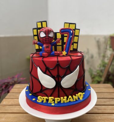 Torta de un piso temática de Spiderman con acabado en fondant, figura 3D de Spiderman en la cima y edificios en fondant.