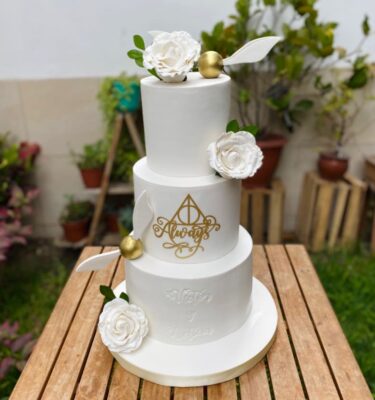 Torta de boda de tres pisos decorada con flores de azúcar en 3D y detalles en fondant, incluyendo una Snitch dorada.
