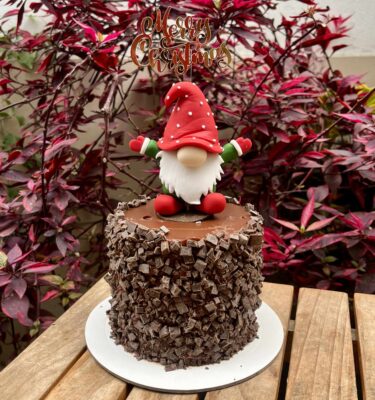 Torta Trocitos bañada en manjar y cubierta con trocitos de chocolate, decorada con un tierno gnomo navideño en 3D