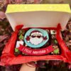 Caja navideña con 20 postrecitos surtidos —trufas, alfajores y brownies— decorada con detalles de Santa Claus en fondant y la frase “Feliz Navidad”