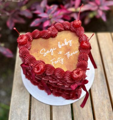 Burncake color rojo vino decorado en buttercream, con cinco cerezas en la parte superior y lazos del mismo color, diseñado para personalizar con imágenes en su interior.