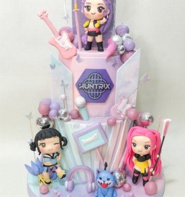 Torta temática de las Huntrix de dos pisos con personajes en 3D, decoraciones pastel y detalles inspirados en el universo K-pop.