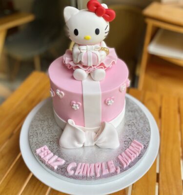 Torta con acabado en fondant, decorada con lazo en fondant y figura 3D de Hello Kitty sosteniendo un regalito en fondant