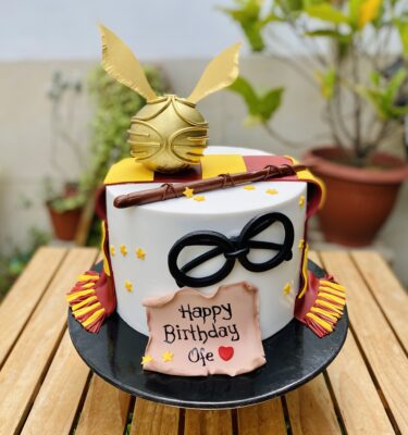 Torta temática de Harry Potter en fondant, decorada con bufanda de Gryffindor, snitch dorada, varita, lentes y pergamino personalizado con nombre.