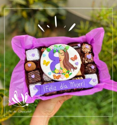 Mix box con postres surtidos y una decoración central del Día de la Mujer con la mitad del número 8 y la mitad del rostro de una mujer.