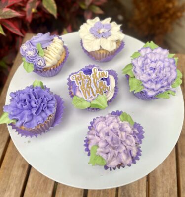 Pack de 6 cupcakes decorados con buttercream lila y blanco, con un topper de “Feliz Día de la Mujer” en uno de los cupcakes.